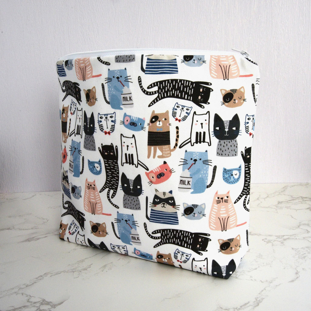 Large and generously sized cat print design wash bag with a 100% cotton outer, closed, standing at an angle, fastening with a quality white nylon zip, and a gusseted boxed bottom, so that it sits upright, placed on a marble surface, with a white background.