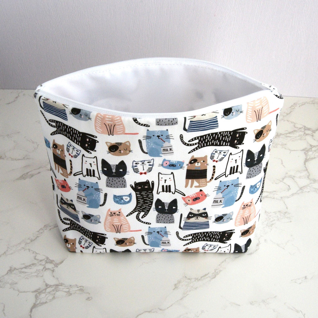 Large and generously sized cat print design wash bag with a 100% cotton outer, open, with a white waterproof PU coated polyester lining, fastening with a quality white nylon zip, and a gusseted boxed bottom, so that it sits upright, placed on a marble surface, with a white background.