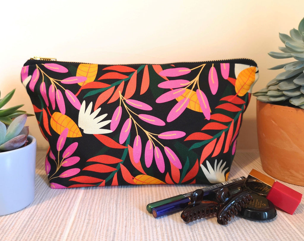Floral brightly coloured wash bag on a bathroom shelf, next to two plants and some make up.