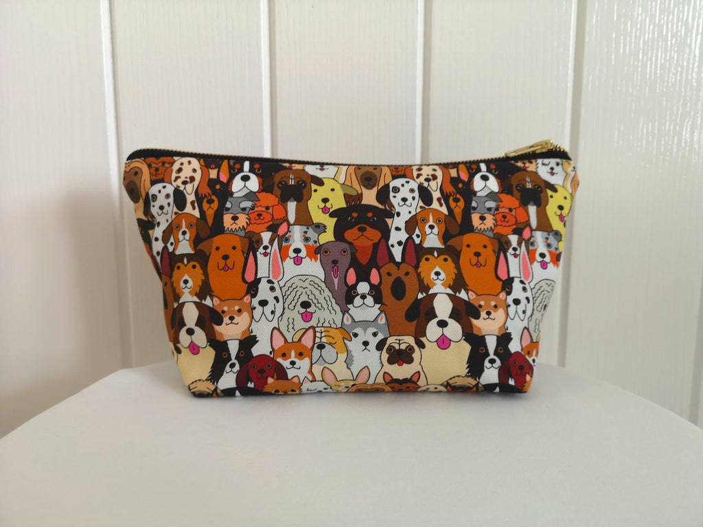 Large Toiletry Wash Bag for Women with stylish Dog print fabric, (the print features lots of different types of dog faces), with a quality brass YKK zip, sitting upright and closed, with zip to the right, with a boxed bottom, on a white table, with a white door in the background.