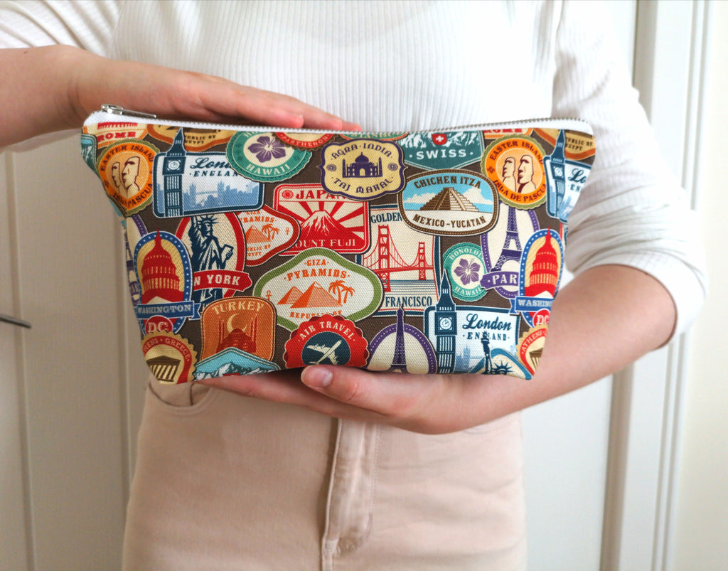 Large Toiletry Wash Bag featuring Travel themed Print, with a quality silver metal YKK zip, closed, held by a woman, to show the scale.