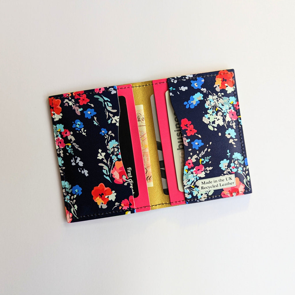 Recycled Leather Folding Wallet Card Holder for women, featuring a Floral pattern on a dark navy blue background, with four slots, with cards and cash in, lying flat on a white background.