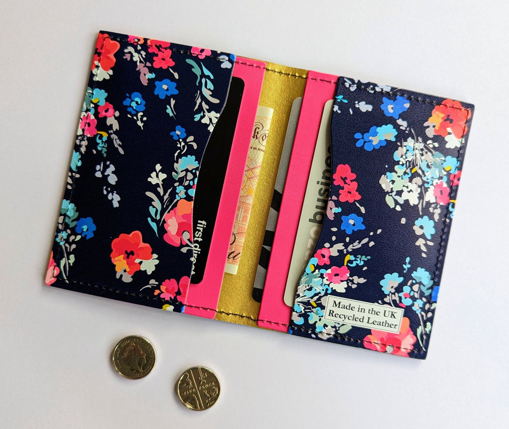 Recycled Leather Folding Wallet Card Holder for women, featuring a Floral pattern on a dark navy blue background, with four slots, with cards and cash in, lying flat on a white background, next to two five pence coins.