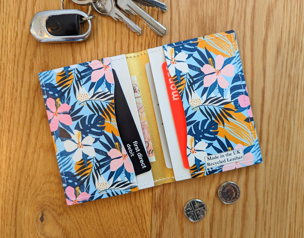 Recycled Leather Folding Wallet Card Holder featuring Tropical Floral Print, with four slots, with cards and cash in, next to keys and two coins, on a wooden surface.