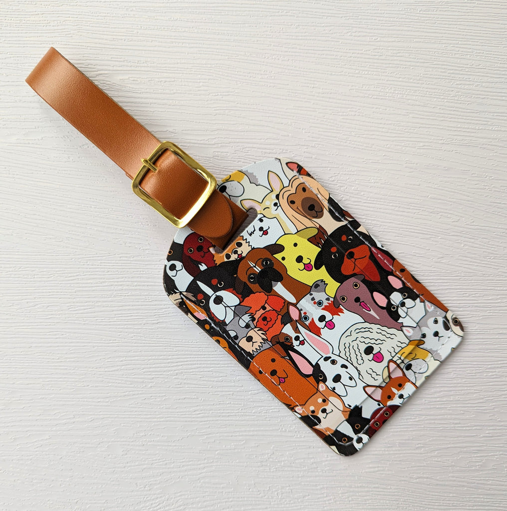 Recycled Leather Luggage Tag featuring dog themed print, with flap covering personal details card, with a strap finished with a sleek gold-plated buckle to attach to luggage, on a white background, lying flat, angled left.