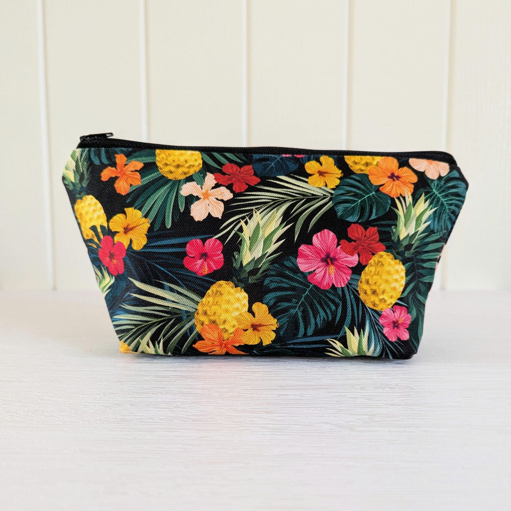 Tropical Makeup Bag featuring tropical pineapple floral print, with a black zip, sitting upright and closed, with zip to the left, with a boxed bottom, on a white background.