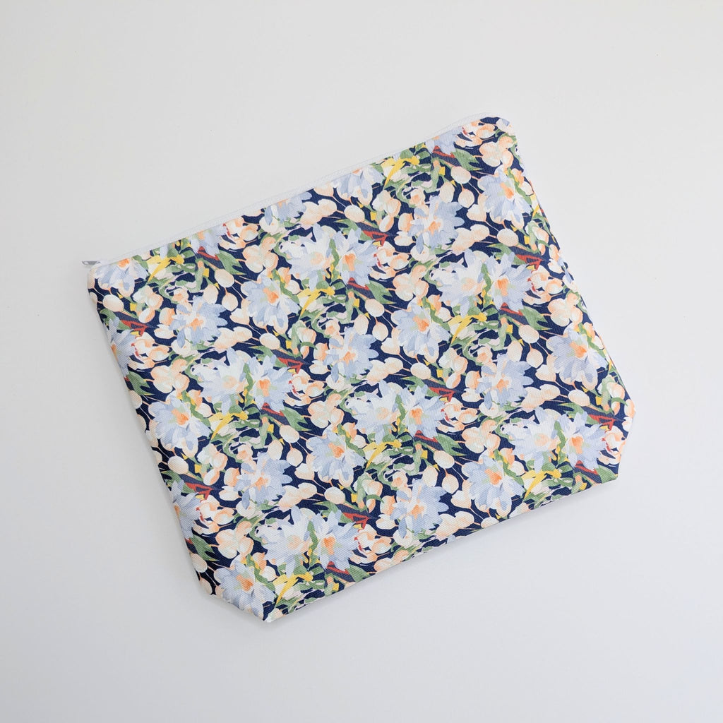 Large Cotton Wash Bag, featuring a stunning blossoming floral pattern design on a dark blue background, with polyester waterproof lining and a quality white nylon zip, on a white background, lying flat, at an angle.