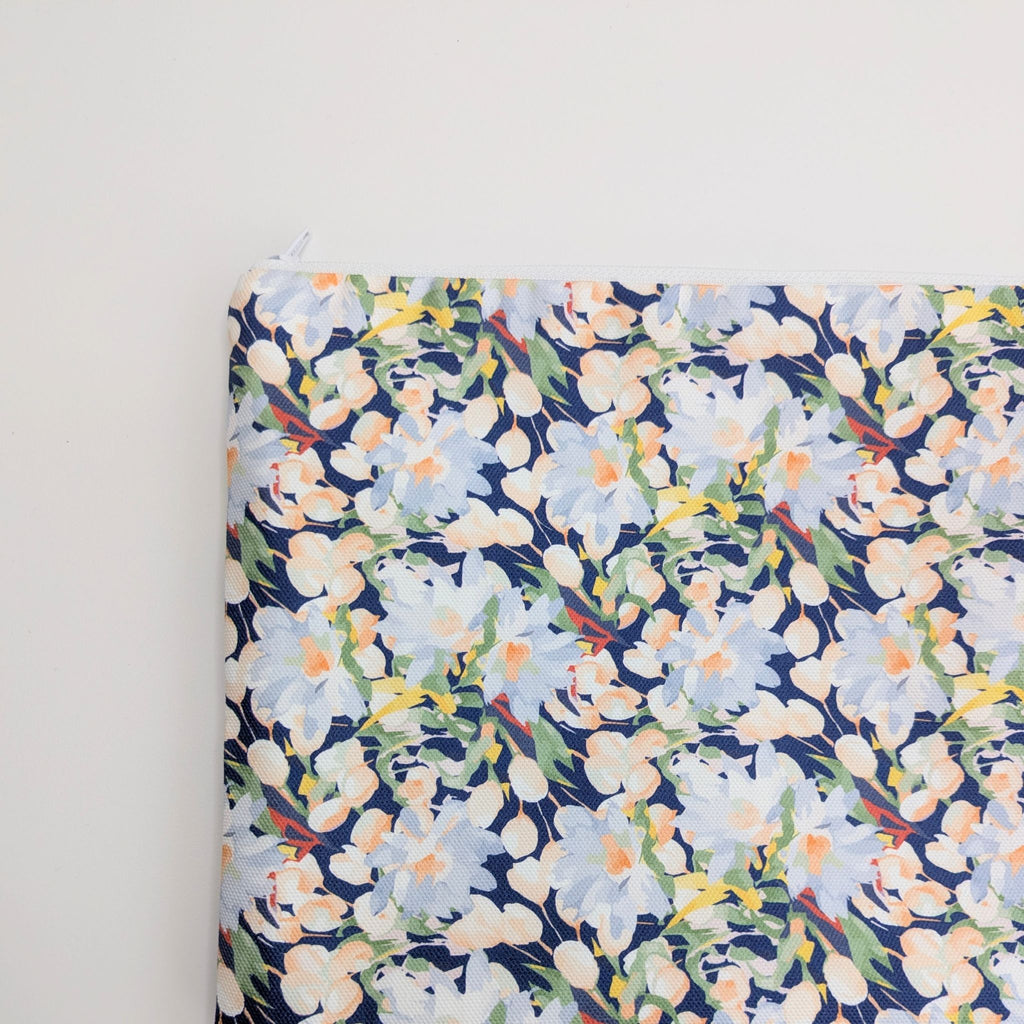 A close up photo of part of a Large Cotton Wash Bag, featuring a stunning blossoming floral pattern design on a dark blue background, with polyester waterproof lining and a quality white nylon zip, on a white background, lying flat.