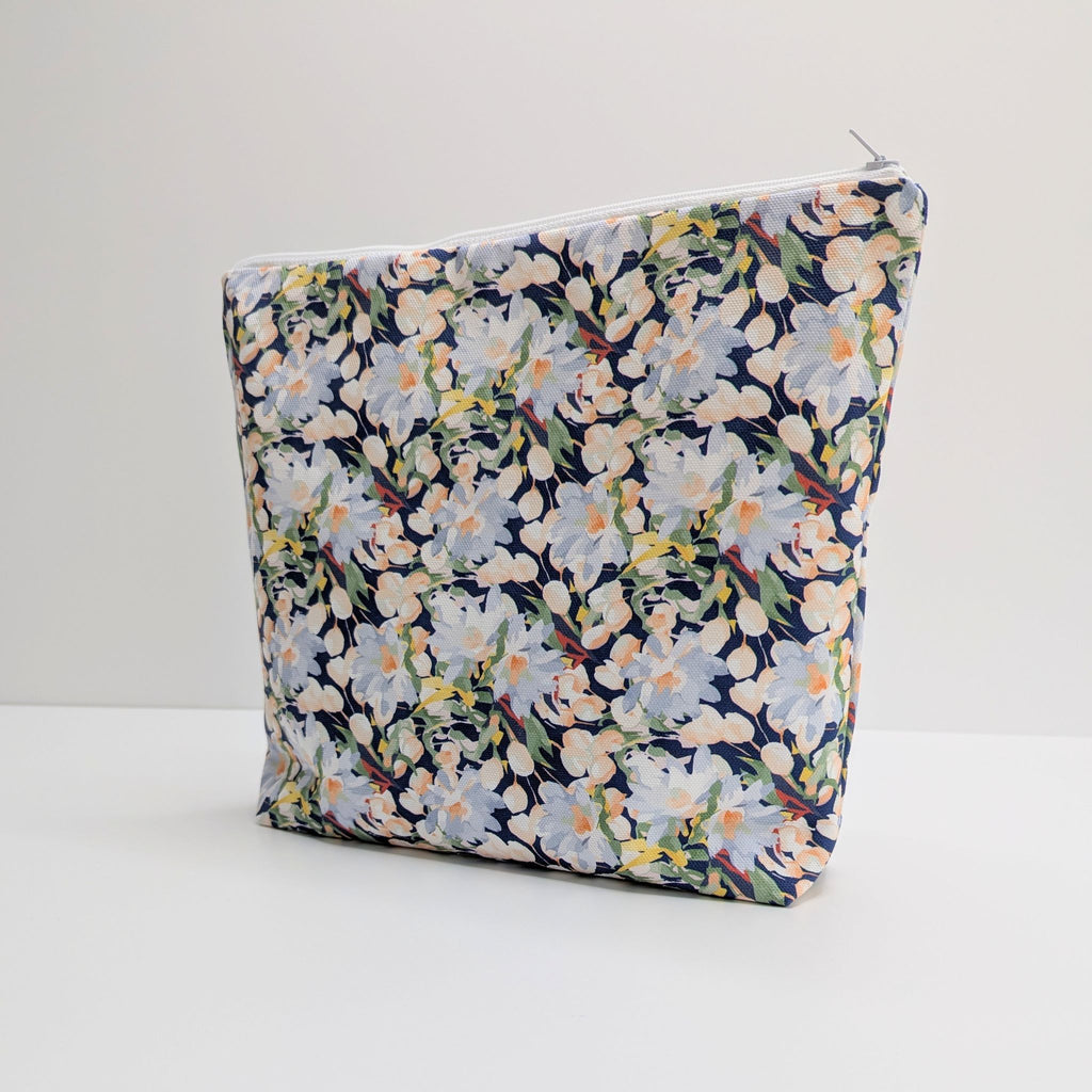 Side view of a Large Cotton Wash Bag, featuring a stunning blossoming floral pattern design on a dark blue background, with polyester waterproof lining and a quality white nylon zip, on a white and grey background.