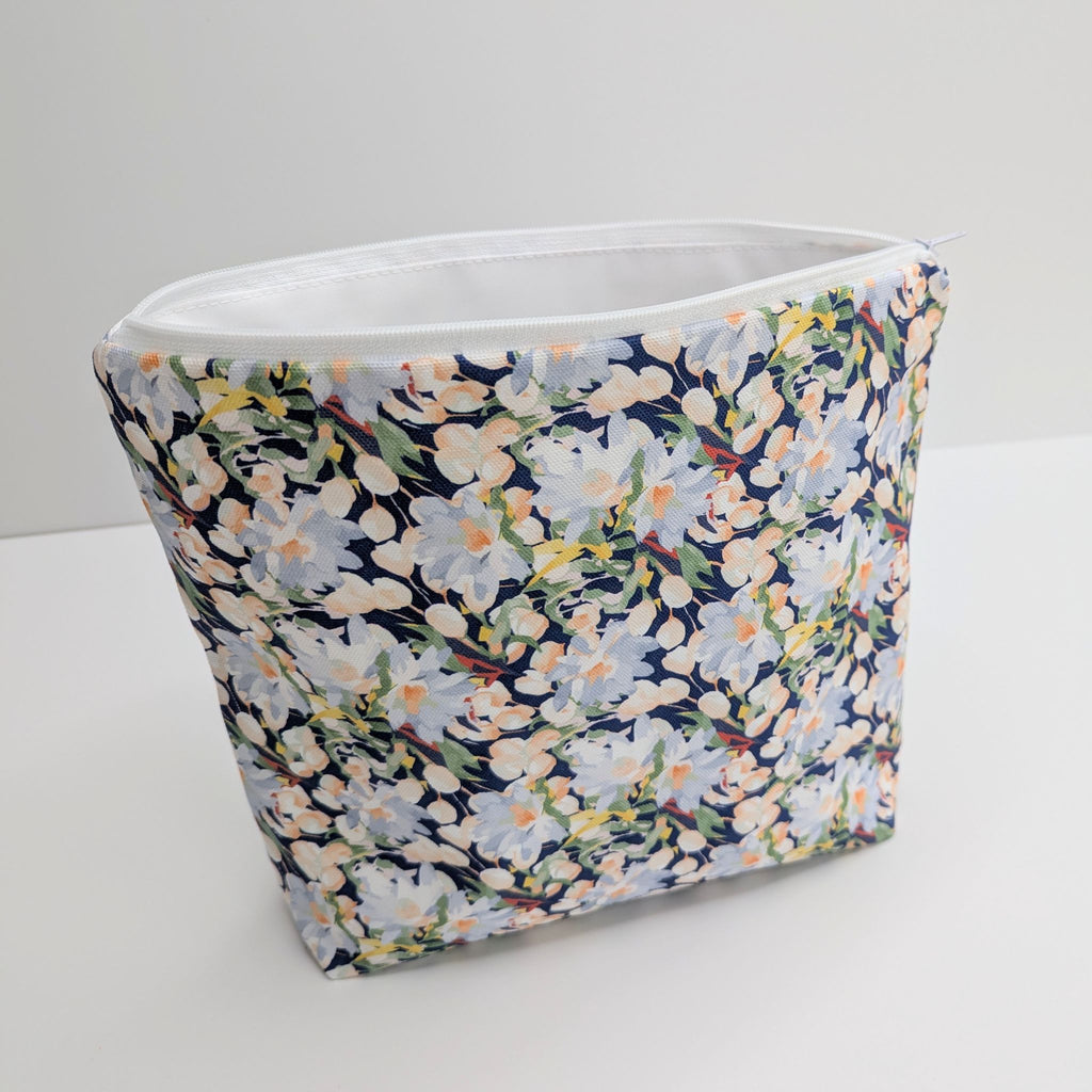 Large Cotton Wash Bag, featuring a stunning blossoming floral pattern design on a dark blue background, with polyester waterproof lining and a quality white nylon zip, on a white background, standing open and upright, at a slight angle, showing some of the lining.
