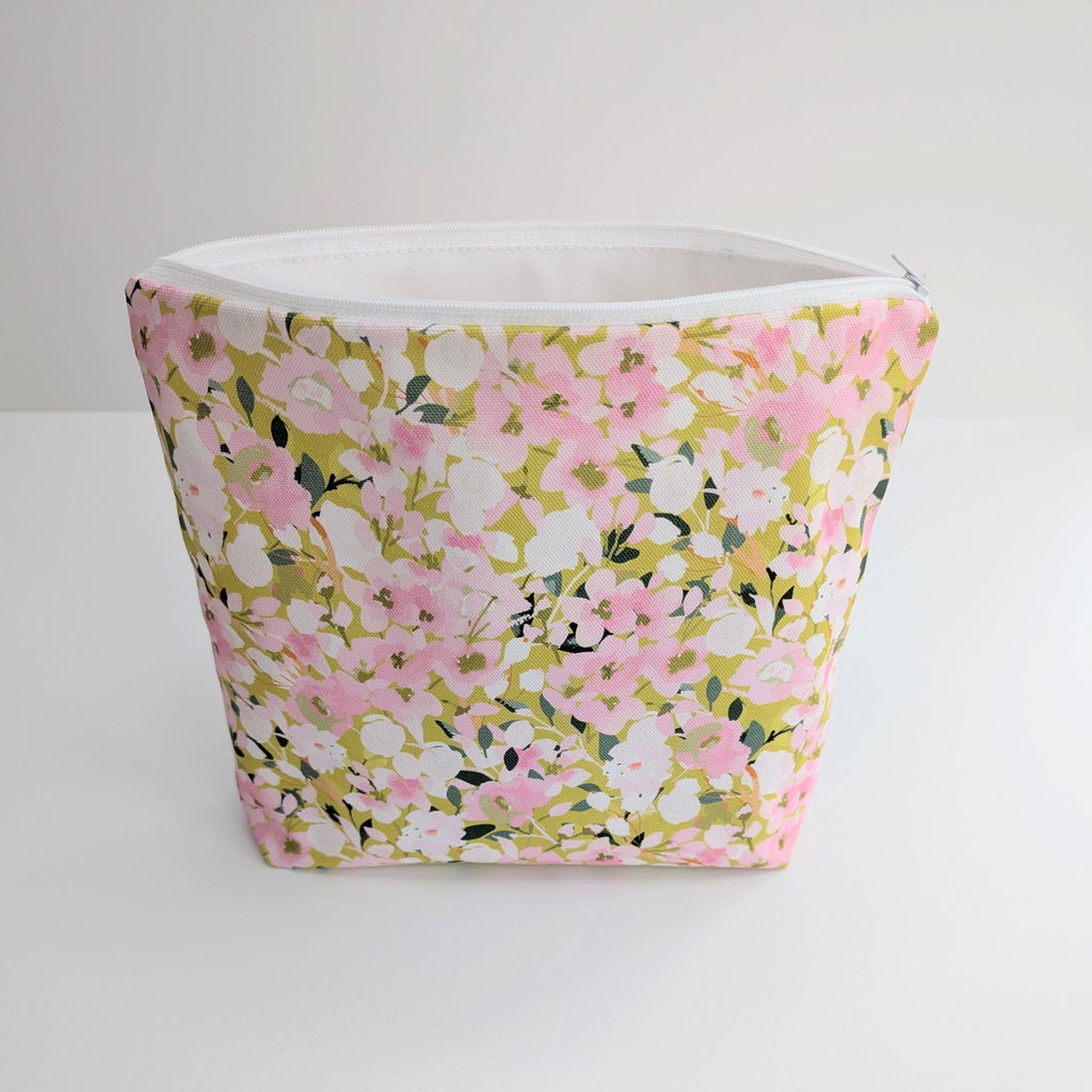 Large Wash Bag, adorned with a stunning cherry blossom floral design, featuring pink cherry blossom on a light green background, open to show a white  waterproof lining and a quality white nylon zip, on a white and grey background.