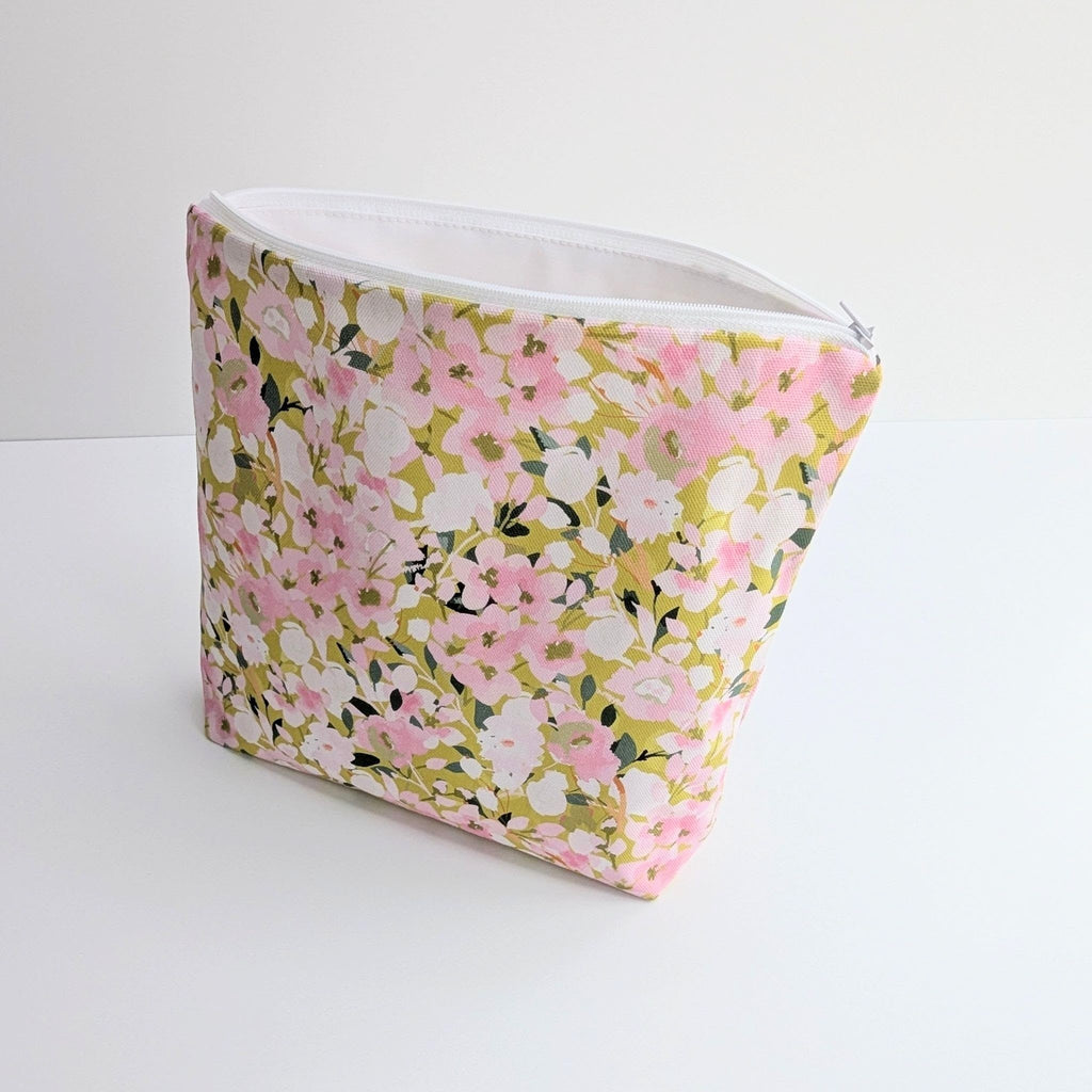 Large Wash Bag, adorned with a stunning cherry blossom floral design, featuring pink cherry blossom on a light green background, open to show a white  waterproof lining and a quality white nylon zip, at angle, on a white and grey background.