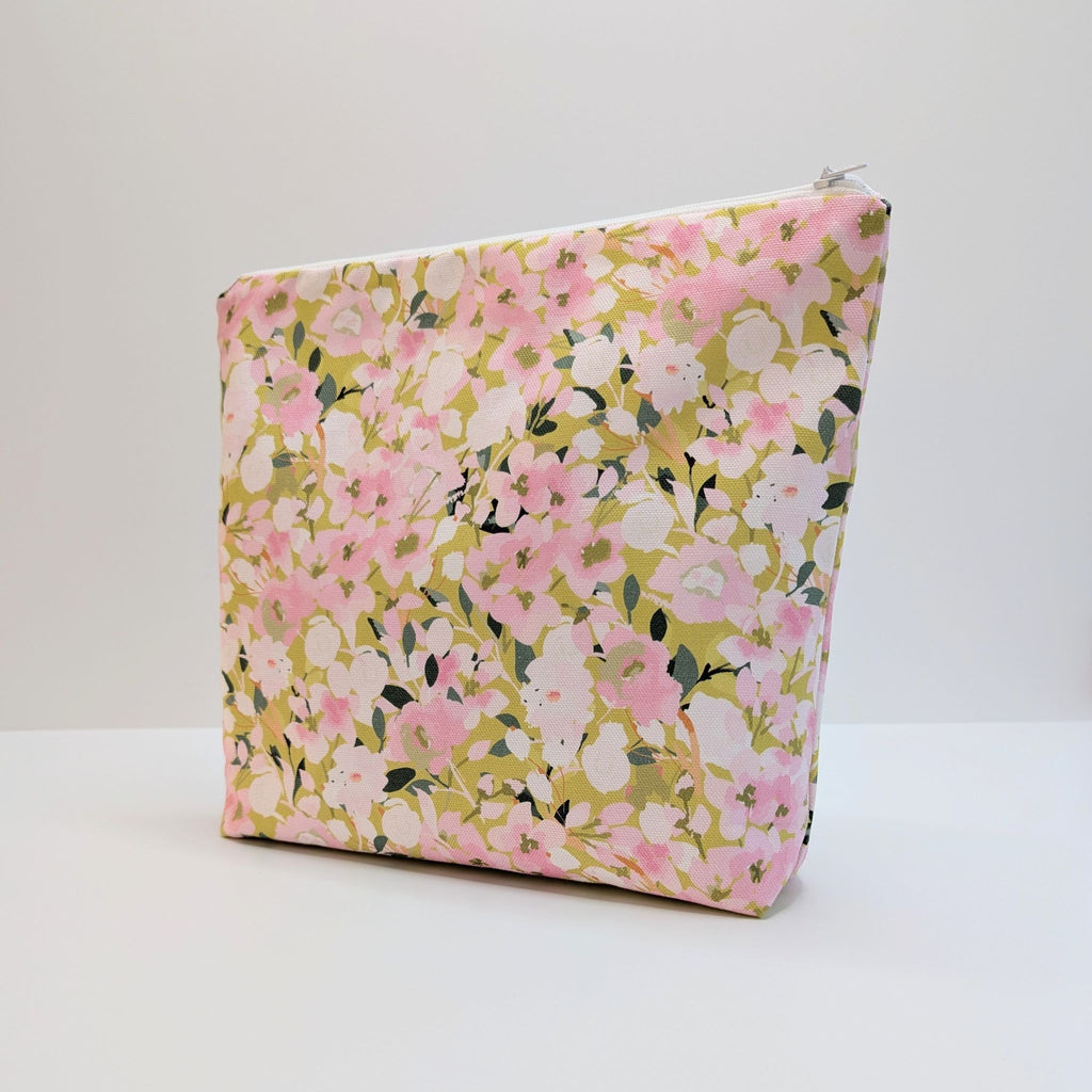 Large Wash Bag, adorned with a stunning cherry blossom floral design, featuring pink cherry blossom on a light green background, with waterproof lining and a quality white nylon zip, standing at an angle, on a white and grey background.