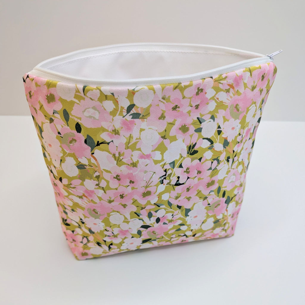 Large Wash Bag, adorned with a stunning cherry blossom floral design, featuring pink cherry blossom on a light green background, open to show a white  waterproof lining and a quality white nylon zip, at angle, on a white and grey background.