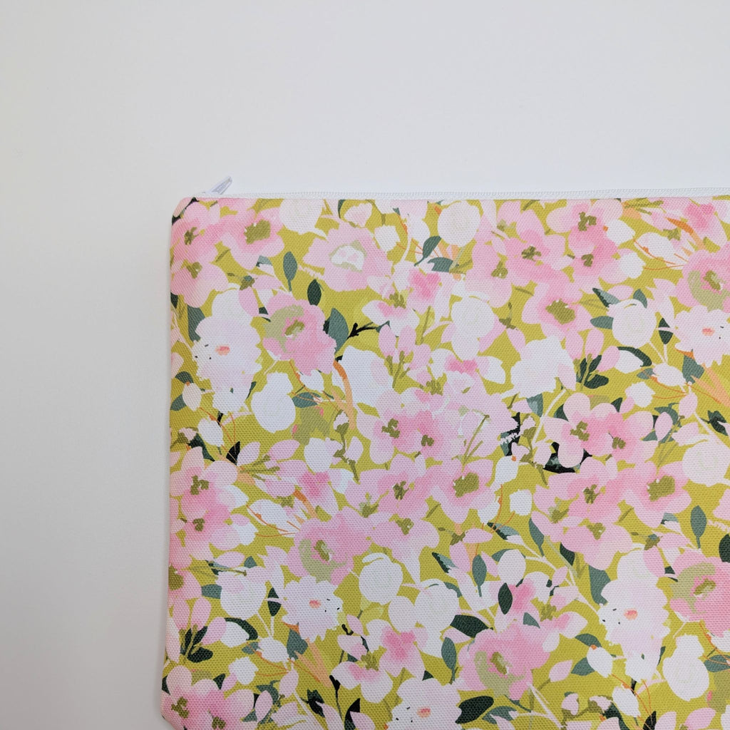 A close up of part of a Large Wash Bag, adorned with a stunning cherry blossom floral design, featuring pink cherry blossom on a light green background, with a quality white nylon zip, lying flat, on a white background.