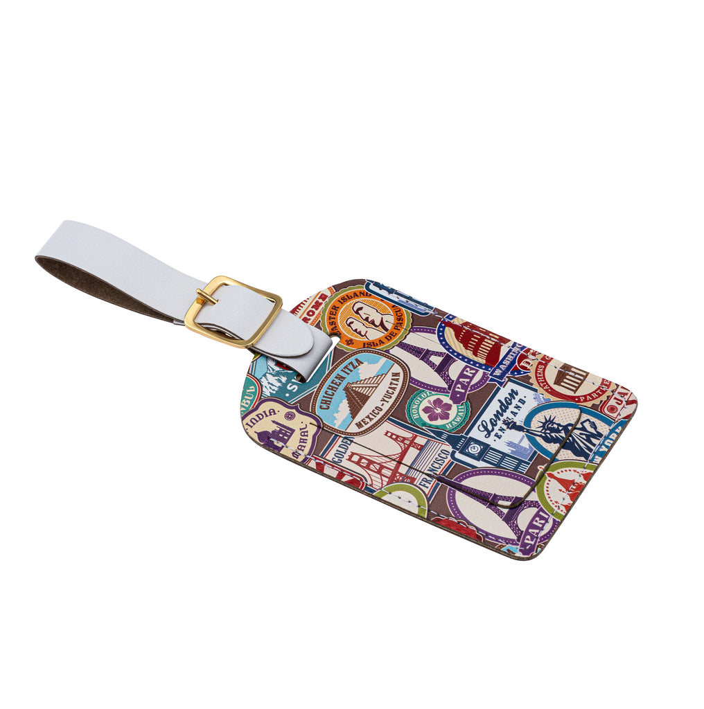 Side view of a recycled Leather Luggage Tag featuring travel themed print, with flap covering personal details card, with a white strap finished with a sleek gold-plated buckle to attach to luggage, on a white background.
