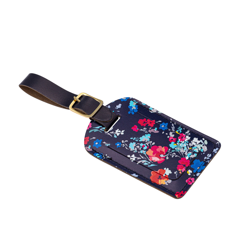 Side view of a recycled Leather Luggage Tag featuring dark blue floral print pattern, with flap covering personal details card, with a strap finished with a sleek gold-plated buckle to attach to luggage, on a white background.