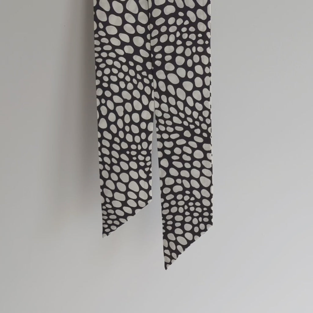 Pure silk satin skinny scarf adorned with a stunning black and white geometric design, hanging on a white background, and lifted to show the details.