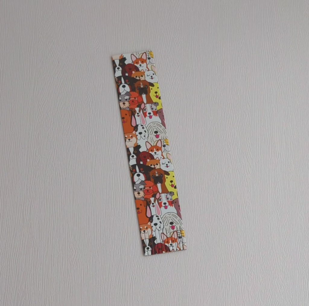 A recycled leather fringed bookmark featuring a colourful dog print pattern lying on a white surface, picked up, turned over and placed inside a book.
