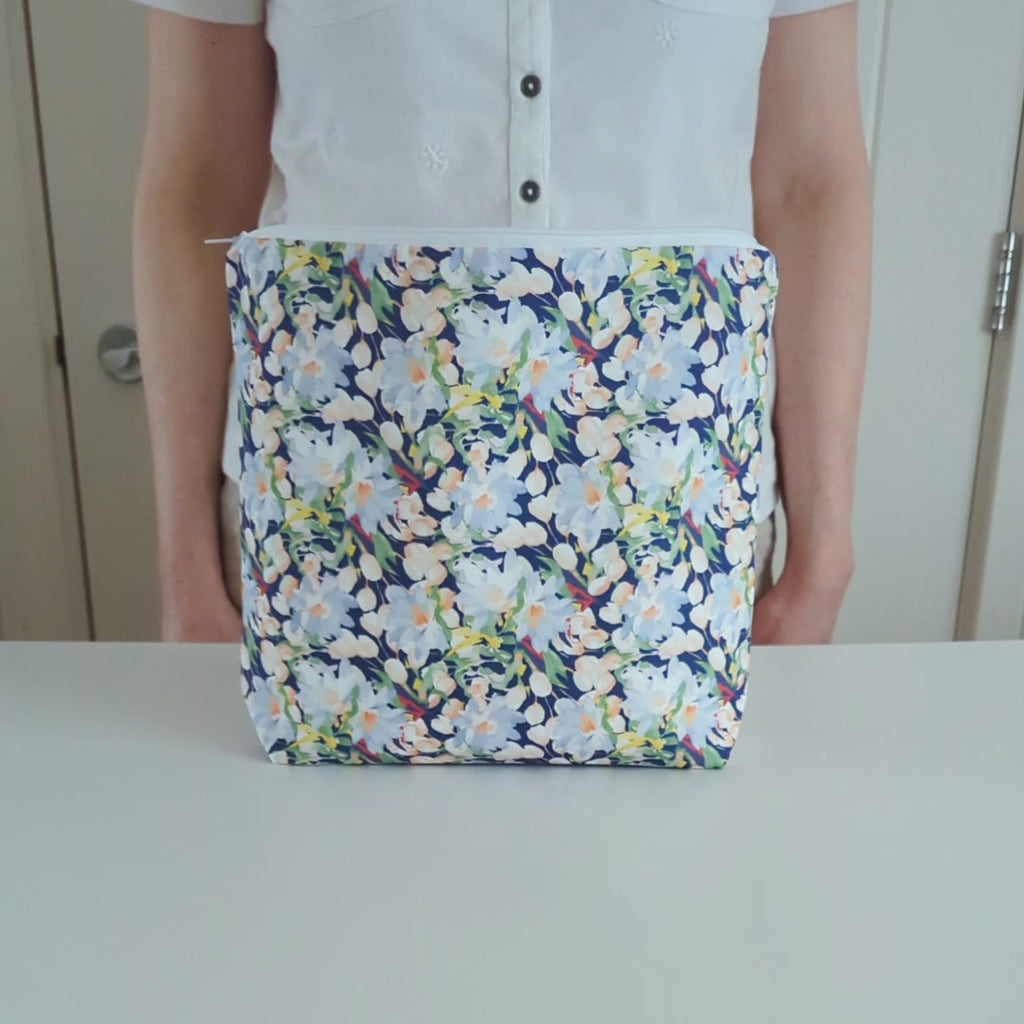 A short video showing a large cotton wash bag, featuring a stunning blossoming floral pattern design on a dark blue background. The wash bag is turned to show both sides, then the inside lining is shown and then the wash bag is zipped up.