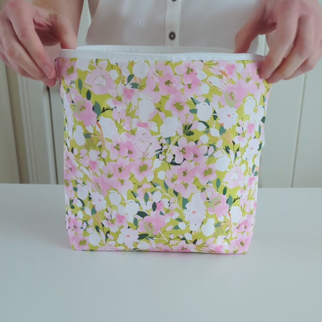 A short video showing a Large Wash Bag, adorned with a stunning cherry blossom floral design, featuring pink cherry blossom on a light green background. The wash bag is turned to show both sides, then the inside lining is shown and then the wash bag is zipped up.