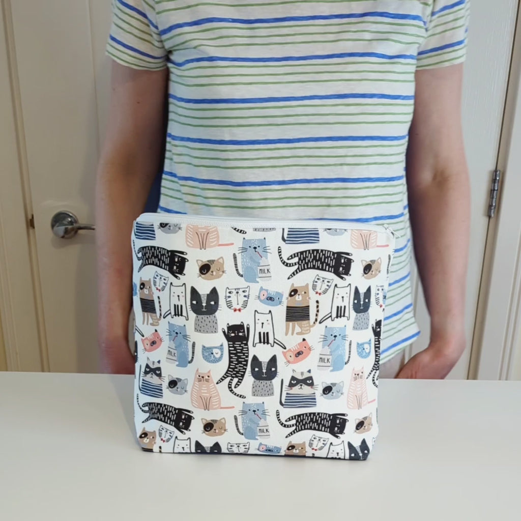 Large and generously sized cat print design wash bag with a 100% cotton outer, rotated and tilted to the side to show the white waterproof PU coated polyester lining inside, and then zipped closed.